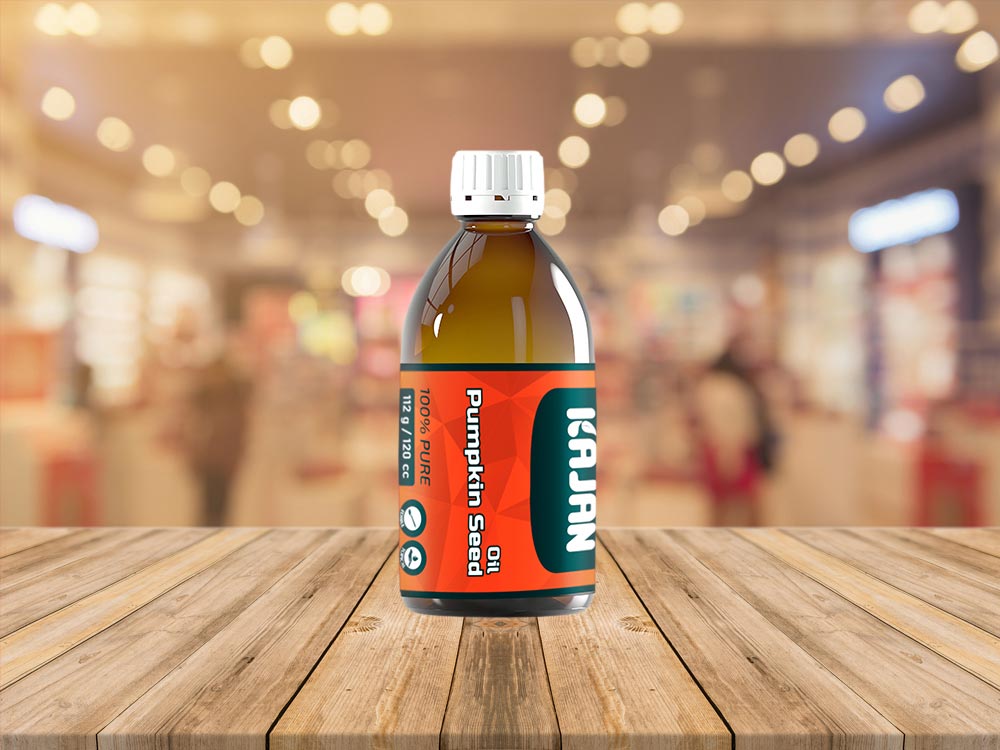 A clear bottle of 100% pure pumpkin seed oil with an orange and teal label, featuring the brand name “KAJAN.”