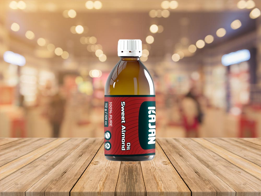 Transparent bottle of KAJAN 100% pure sweet almond oil with a red label and white cap, set against a white background.