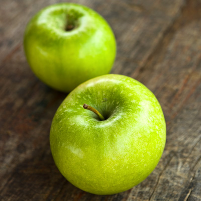 Two green Granny Smith apples displayed on a wooden table surface.