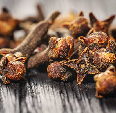  Dried cloves placed on a wooden table, emphasizing their dark hue and distinct, spiky appearance.

