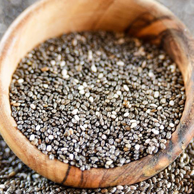 Chia seeds are displayed in a rustic wooden bowl, showcasing their tiny, black, and white speckled appearance.