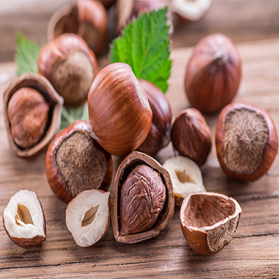A wooden table displaying hazelnuts and vibrant green leaves scattered around.
