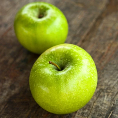 Two green Granny Smith apples displayed on a wooden table surface.
