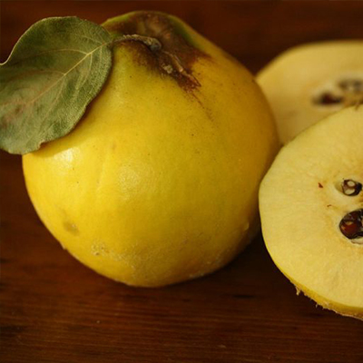 A yellow quince, sliced in half, displaying its soft interior, accompanied by fresh green leaves.
